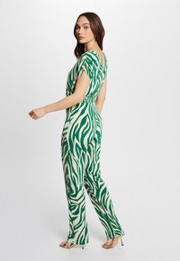 Grønt og creme zebra-mønster jumpsuit med korte ærmer, indsnøret talje og brede bukser. Glat stof og elegant silhuet.