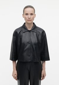 Zwarte leren cropped jack met een brede kraag, korte mouwen en een sluiting met knopen aan de voorkant, met een gladde textuur en een minimaal ontwerp.