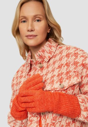 Orange gestrickte Handschuhe mit gerippten Bündchen, kombiniert mit einer gemusterten rot-beigen Hahnentrittbluse. Weicher Stoff, warmes Design.