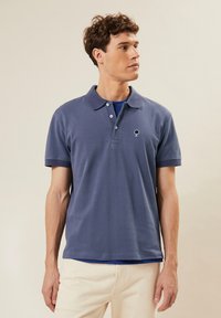 Donkerblauwe polo shirt van katoen, met een klassieke kraag, een drieknopenpad en een klein boomlogo op de borst.