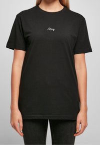 Černé bavlněné tričko s krátkým rukávem a kulatým výstřihem, se malým bílým kurzívním logem na levé straně hrudi.