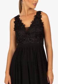 Abito nero con profondo scollo a V, decorato con un intricato inserti in pizzo, pannello semi-trasparente e una gonna fluida e arricciata.