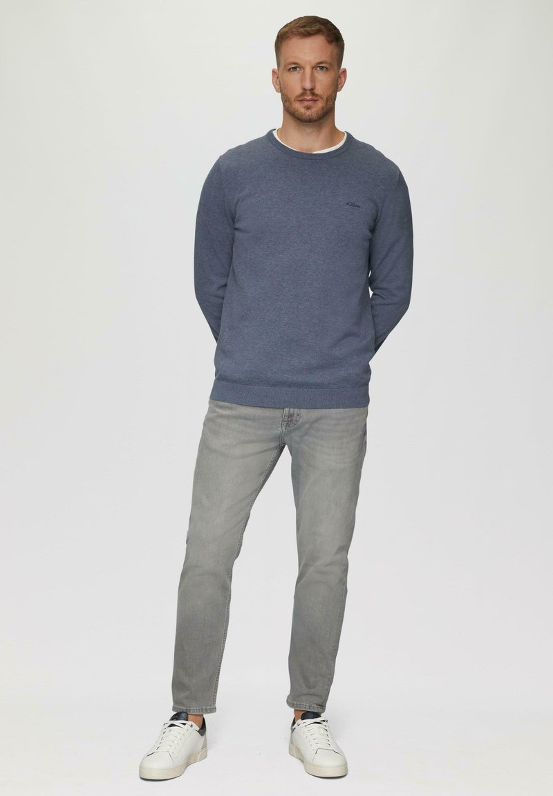 Tumši zila sporta sega ar apaļu kakla izgriezumu, apvienota ar gaiši pelēkām džinsām un baltām kedām. Vienkāršs dizains, strukturēta auduma, minimāla zīmola atzīme.