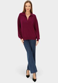 Bordowy sweter z dzianiny z kołnierzykiem, o luźnym kroju. W zestawieniu z ciemnoniebieskimi, dzwoniastymi dżinsami i czarnymi butami na wysokim obcasie.