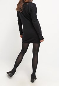 Abito a maglia nero con maniche lunghe, caratterizzato da una forma rilassata e un orlo sopra la metà della coscia; abbinato a collant neri opachi e tacchi neri.