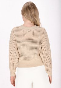 Beżowy sweter z dzianiny o luźnym, otwartym splotcie, z prążkowanymi mankietami, szerokim dekoltem i obniżonymi szwami na ramionach.
