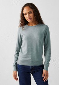 Lichtgrijze trui van zachte stof, met een ronde hals, lange mouwen en ribgebreide manchetten. Gepaard met donkerblauwe jeans.