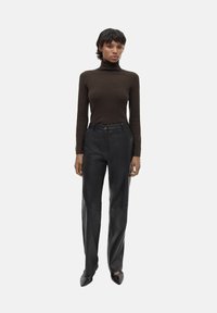 Brauner Rollkragenpullover und schwarze Lederhose. Die Hose hat einen geraden Schnitt mit Einsätzen. Das Modell trägt spitze schwarze Schuhe.