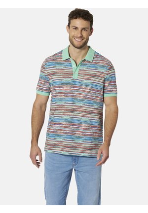Lächelnder Mann, der ein mehrfarbig gestreiftes Poloshirt mit mintgrünem Kragen und Bündchen trägt, kombiniert mit hellblauen Jeans, vor weißem Hintergrund stehend.