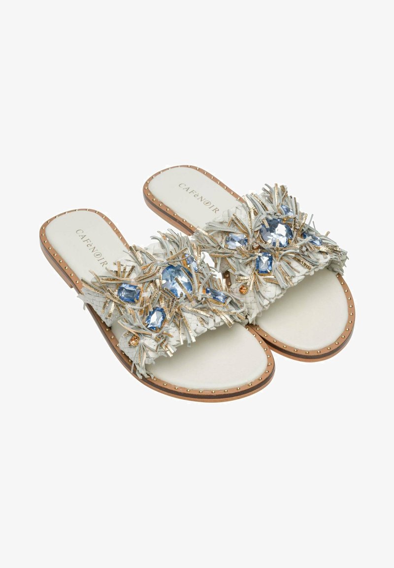 Sandales blanches à enfiler avec une bride texturée à franges ornée de pierres précieuses bleues, d'accentuations dorées et de détails cloutés sur la semelle.