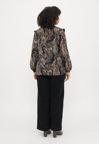 Blusa preta de manga longa com padrão de folhas bege, ombros bufantes e detalhes em babados, combinada com calças pretas de perna larga e saltos cinzas.