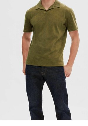 Polo de manga corta verde oliva con cuello plano, hecho de tejido texturizado. Combinado con jeans de mezclilla azul oscuro con costuras en contraste.