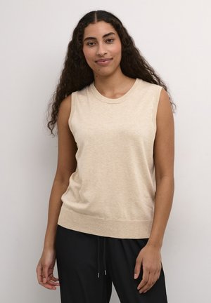 Haut tricot beige sans manches avec un col rond et un ourlet côtelé. Le tissu semble doux avec une texture subtile. Porté avec un pantalon noir.