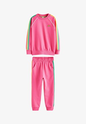 Rózsaszín pulóver és nadrág szett szivárványos részletekkel. Puha anyag, laza szabás, bordás mandzsetták. Színes sportcipők teszik teljessé az öltözetet.