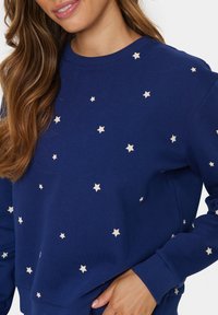 Felpa marina con motivi a stelle chiare sparsi. Caratterizzata da un collo a giro e polsini a coste. Realizzata in un morbido mix di cotone.