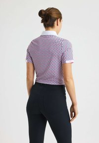 Kurzärmliges Poloshirt im pinken und blauen geometrischen Muster mit weißem Kragen, kombiniert mit schwarzen Slim-Fit-Hosen mit Gesäßtaschen.