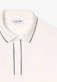 Vit Lacoste polo skjorta med en texturerad väv, en klassisk krage och en kontrasterande marinblå trim längs knäppningen och kragen, samt varumärkeslogotypen på bröstet.