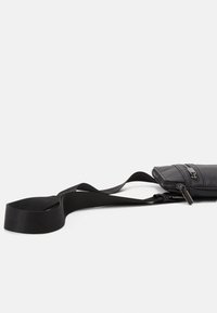 Černá kožená kabelka přes rameno s texturovaným povrchem, vybavená zipovým uzávěrem a nastavitelným popruhem. Kompaktní design s funkčními detaily.