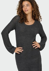 Robe en tricot à manches longues de couleur gris foncé. Elle présente un col arrondi et un tissu texturé avec une coupe décontractée et des poignets côtelés.