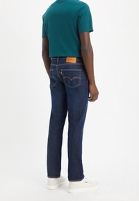 Mörkblå denimjeans med rak passform, med orange sömmar och klassiska bakfickor, kombinerat med en teal kortärmad skjorta.
