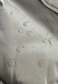 Des gouttes d'eau perlent sur un tissu imperméable lisse de couleur gris clair, avec une couture visible dans le coin supérieur droit.