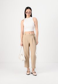 Hvit ermløs crop topp, beige høytlivsbukser med knyte detalj, hvit veske og beige sko med stropper. Glatte teksturer.