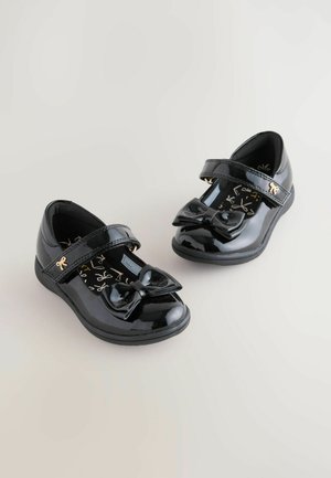 Zwarte gepatineerde leren schoenen met een ronde neus, voorzien van een strik aan de voorkant en een klittenbandsluiting. Het interieur heeft een gouden scriptpatroon.
