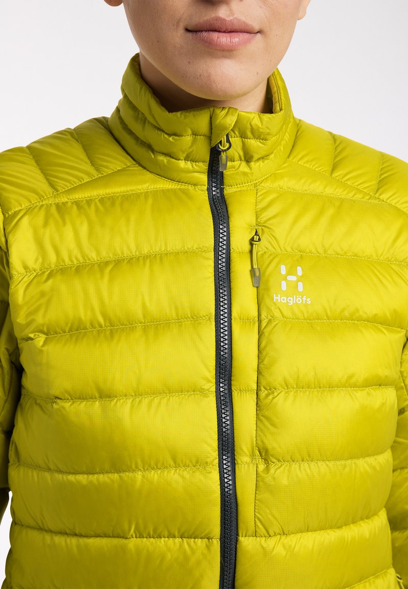 Helle gelbe isolierte Jacke mit hohem Kragen, versehen mit vertikalen Steppmustern und einem Reißverschluss in kontrastierendem Dunkelgrau.