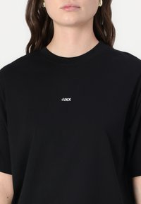 Black cotton t-shirt featuring a crew neck and short sleeves. The front has a small white logo text "JJXX" centered below the neckline.