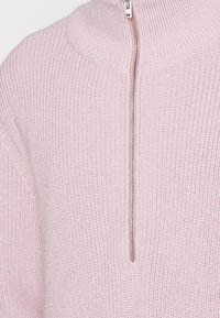 Jasnoróżowy sweter z dzianiny z wysokim kołnierzem i półzamkiem, z teksturowanym materiałem i żebrowanym wykończeniem.