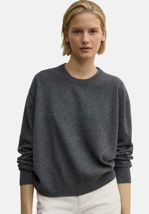 Pull en gris foncé à manches longues, col et ourlet côtelés, texture douce, coupe décontractée, porté avec un pantalon blanc.