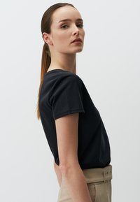 Czarna bawełniana koszulka z krótkim rękawem i okrągłym dekoltem, noszona włożona w khaki spodnie o wysokim stanie z paskiem w talii.