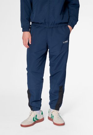 Navy track pants made from lightweight material, featuring elastic cuffs, side pockets, and black accents along the legs. Branded logo visible.