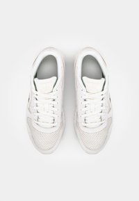 White sneakers with a perforated leather upper, flat laces, a padded collar, and textured rubber sole. Branding on the tongue.