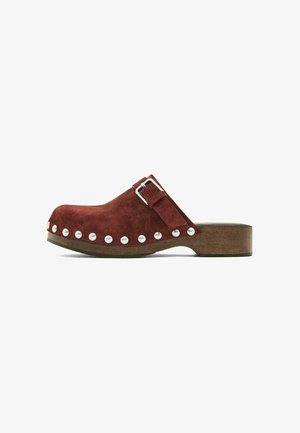 Sabot en daim marron avec semelle en bois, boucle argentée sur le côté et clous argentés le long du bord inférieur de la tige.