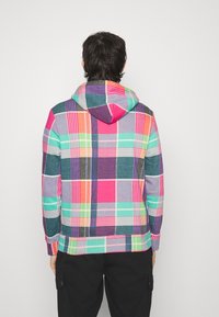 Sudadera de cuadros multicolores con capucha, que presenta patrones vibrantes en rosa, verde, morado y naranja. Hecha de una tela suave y texturizada.
