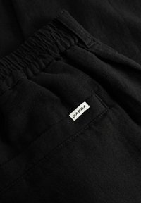 Crne hlače s elastičnim strukom na kojem je prišivena mala bijela tkanina s natpisom "GABBA" blizu šava džepa.