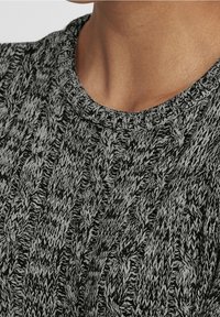 Pull en maille avec un motif noir et gris, présentant un design de câble texturé et un col rond. Matière douce de poids moyen.
