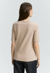 Beige T-Shirt mit kurzen Ärmeln und Rundhalsausschnitt, weicher Textur und einfachem Design, kombiniert mit dunkelblauen Jeans.