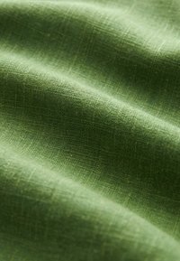 Grön texturerad tyg med ett subtilt vävt mönster, med en mjuk, något glansig yta och en varierande nyans av grönt.