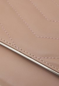 Světle růžová syntetická kůže s diagonálními švy a metalickým akcentem podél okraje. Hladký povrch a minimalistický design.