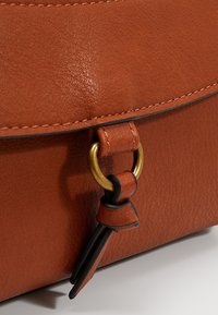 Borsa in pelle marrone con superficie testurizzata, dettagli in ottone dorato e fibbia distintiva. Include un portachiavi decorativo.