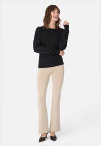 Černý pletený svetr s kulatým výstřihem, dlouhými rukávy a žebrovanými manžetami, v kombinaci s světle béžovými rozšířenými kalhotami a černými lodičkami.