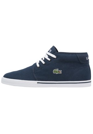 Granatowe sneakersy z płótna z średnią cholewką, białymi sznurowadłami, białą gumową podeszwą i zielonym logo krokodyla po boku.