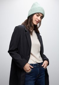 Jasnoszara dziana czapka, czarny dopasowany płaszcz, beżowy sweter i niebieskie dżinsy. Skup się na fakturze i warstwowym wyglądzie.