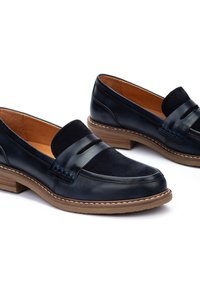 Mocasines de cuero negro con un acento de ante, que presentan una suela cosida, punta redonda y tacón de goma marrón. Diseño clásico para uso casual.
