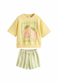 Top galben din bumbac cu mâneci scurte și grafică cu pară, asortat cu pantaloni scurți verde și albi cu dungi, având talie elastică și detaliu cu funda.