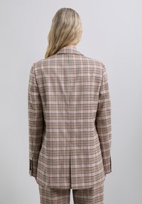 Pink and beige plaid blazer, tailored fit with a notched lapel, two-button front, and back vent. Smooth texture with contrasting green lines.
