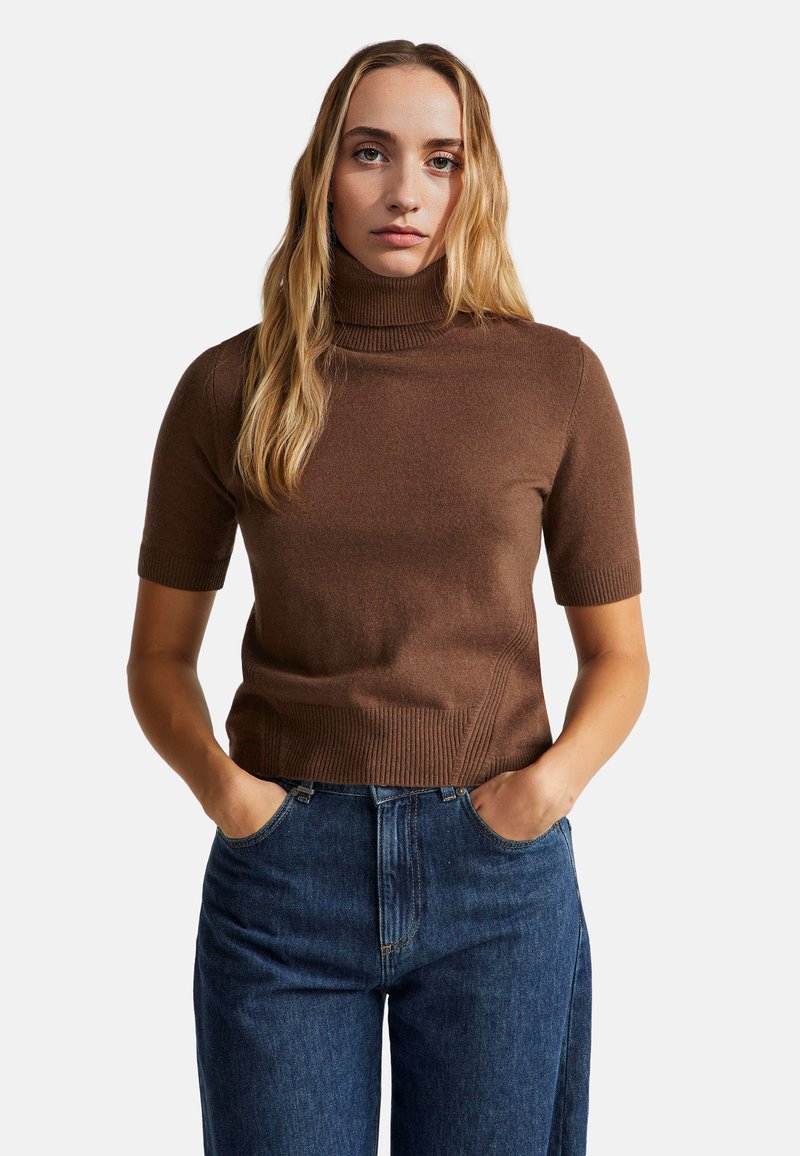 Hnědý krátkosrstý rolák s žebrovanou strukturou, přiléhavý design a rovný lem, v kombinaci s modrými džíny s vysokým pasem.