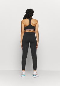 Svart sport-bh med rosa accentstrimmor och svarta högmidjade leggings. Modell som bär vita sneakers med turkosa och persikofärgade accenter.